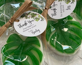 May include: A translucent green monstera leaf-shaped soap packaged in a clear plastic bag with a brown paper tie and a round white tag. The tag features a botanical illustration and the text Thank You From Bailey's Shower to yours! Love, Bailey.