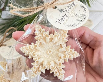 May include: A white snowflake ornament with intricate details is packaged in a clear plastic bag with a brown twine bow. A round tag with the text "Happy Holidays from the Andersons 2024" is attached to the bag.