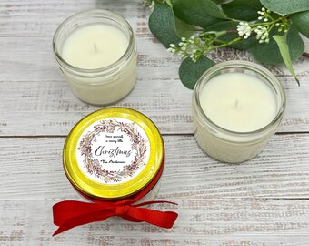 May include: Two small glass jars with white candles and gold lids. The lid of one jar has a white label with a red and brown wreath design and the text "Have yourself a merry little Christmas The Andersons".