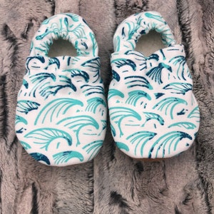 May include: A pair of white baby booties with a blue and green wave pattern.