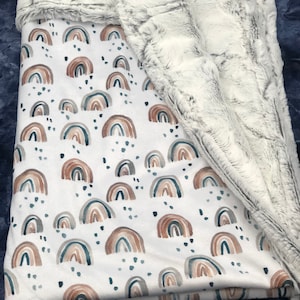 May include: A soft, white and gray faux fur baby blanket with a white cotton side featuring a repeating pattern of watercolor rainbows in shades of brown, teal, and gray.