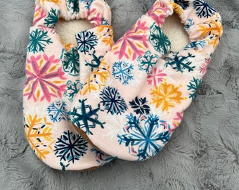 May include: A pair of pink slipper socks with a snowflake pattern in shades of blue, yellow, and pink. The socks have a white fleece lining.
