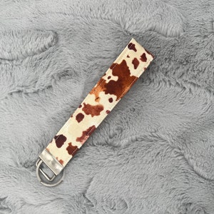 May include: A brown and white cow print key chain with a silver metal ring.