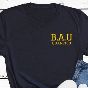 May include: A navy blue t-shirt with a yellow graphic that says "B.A.U. Quantico"