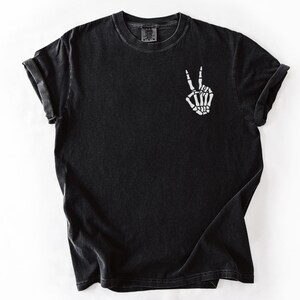 K&ouml;nnte beinhalten: Schwarzes T-Shirt mit kurzen &Auml;rmeln und Rundhalsausschnitt. Das Shirt zeigt eine wei&szlig;e Skeletthand, die ein Friedenszeichen auf der Vorderseite macht. Der Stoff hat einen leicht verblichenen, Vintage-Look.