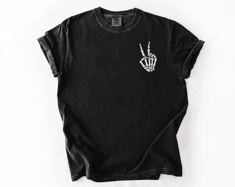 K&ouml;nnte beinhalten: Schwarzes T-Shirt mit kurzen &Auml;rmeln und Rundhalsausschnitt. Das Shirt zeigt eine wei&szlig;e Skeletthand, die ein Friedenszeichen auf der Vorderseite macht. Der Stoff hat einen leicht verblichenen, Vintage-Look.