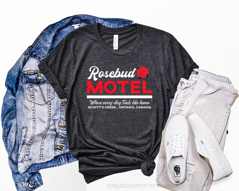 May include: A dark grey t-shirt with a red graphic that says "Rosebud Motel" with a red rose. The text below says "Where every stay feels like home" and "Schitt's Creek, Ontario, Canada".