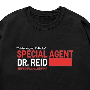 May include: Black sweatshirt featuring the text "This is calm, and it's Doctor" above "SPECIAL AGENT DR. REID" in white and red. The words "BEHAVIORAL ANALYSIS UNIT" are below in white.