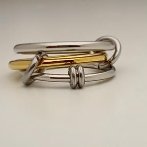 Op de afbeelding: Een zilveren en gouden ring met een gedraaid ontwerp. De ring is gemaakt van drie banden, twee zilveren en een gouden, die met elkaar zijn verweven.