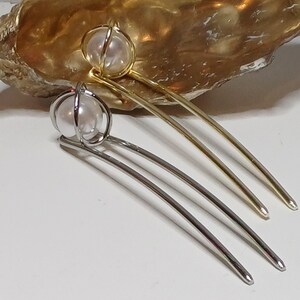 Puede incluir: Dos pinzas para el pelo con detalles de perlas. Las pinzas son de metal y tienen una forma curva. Una pinza es dorada y la otra es plateada.