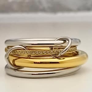 Könnte beinhalten: Ein mehrreihiger Ring mit einem goldenen Band, einem silbernen Band und einem Band mit kleinen Diamanten. Die Bänder sind ineinander verschlungen und der Ring hat ein einzigartiges Design.