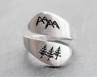 May include: A silver ring with a mountain and tree design. The ring is split into two parts, with the mountains on one side and the trees on the other.