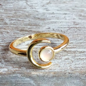 May include: A gold ring with a crescent moon design and a white gemstone in the center.