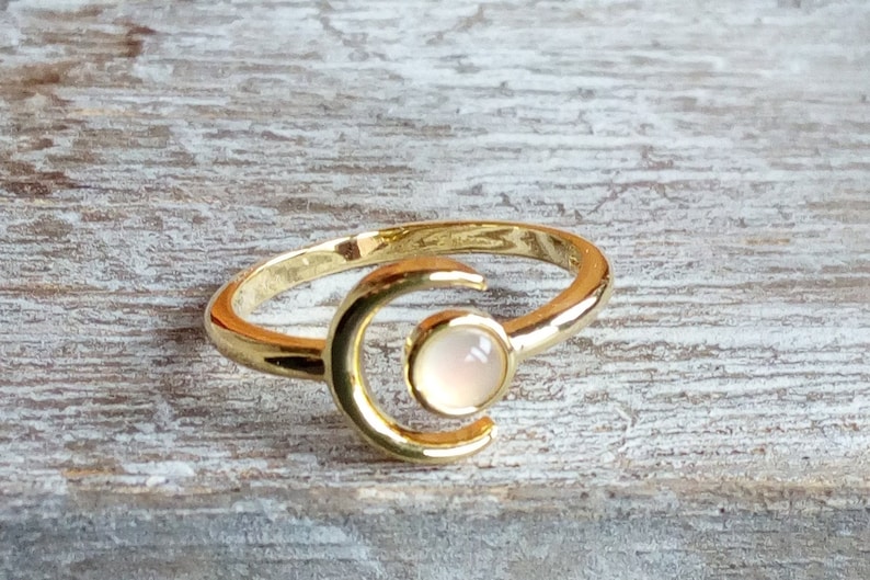 May include: A gold ring with a crescent moon design and a white gemstone in the center.