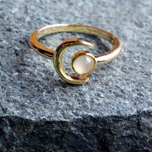 May include: A gold ring with a crescent moon design and a white stone in the center.