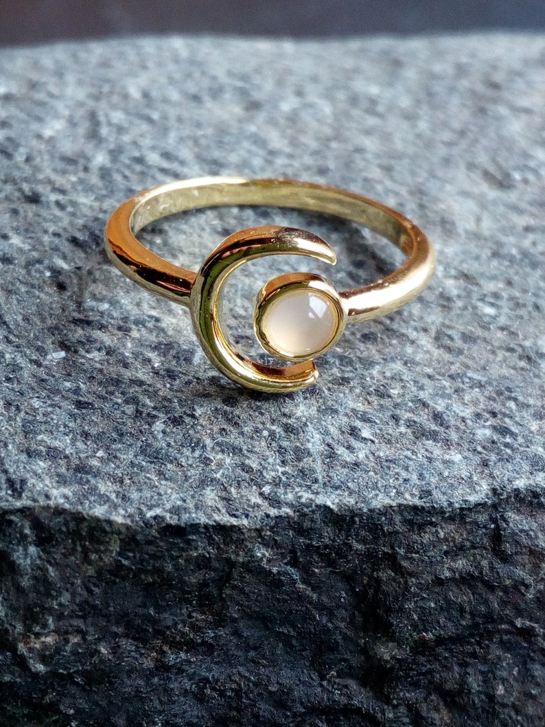 May include: A gold ring with a crescent moon design and a white stone in the center.