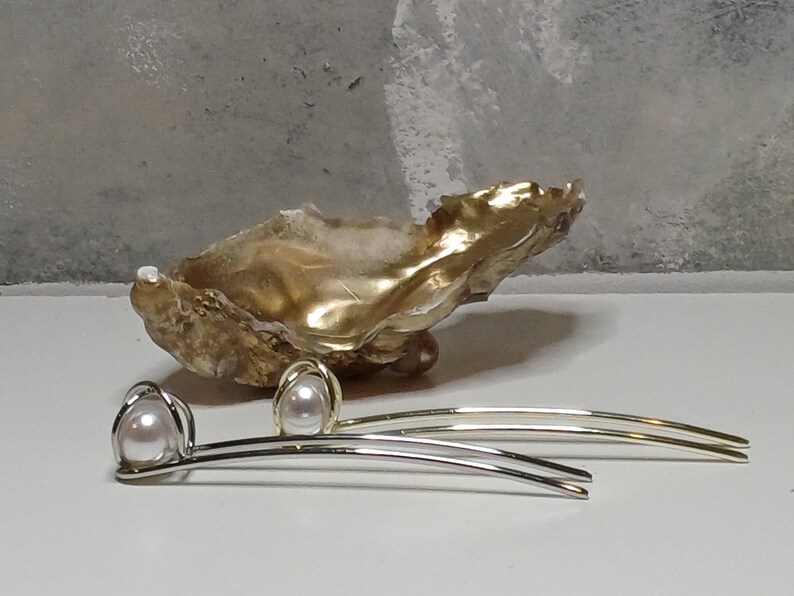 Puede incluir: Dos pinzas para el pelo plateadas con un acento de perla. Las pinzas son curvadas y tienen un dise&ntilde;o simple. Las perlas son blancas y redondas.