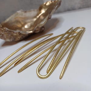 Op de afbeelding: Set van vier gouden haarspelden met een gebogen vorm. De spelden zijn in een kruispatroon gerangschikt.