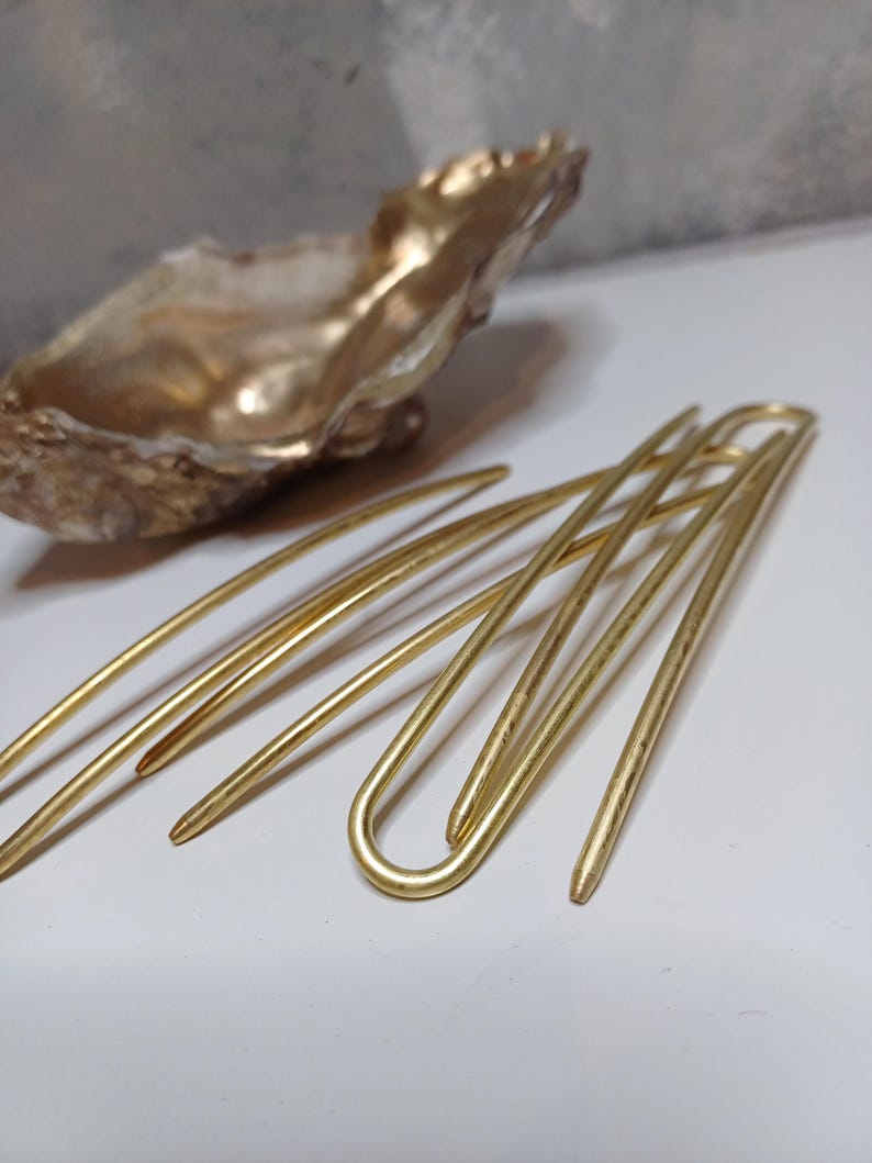 Op de afbeelding: Set van vier gouden haarspelden met een gebogen vorm. De spelden zijn in een kruispatroon gerangschikt.