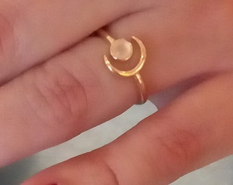 May include: A gold ring with a crescent moon design and a white stone in the center.