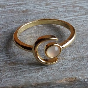 May include: A gold ring with a crescent moon design and a white gemstone in the center.