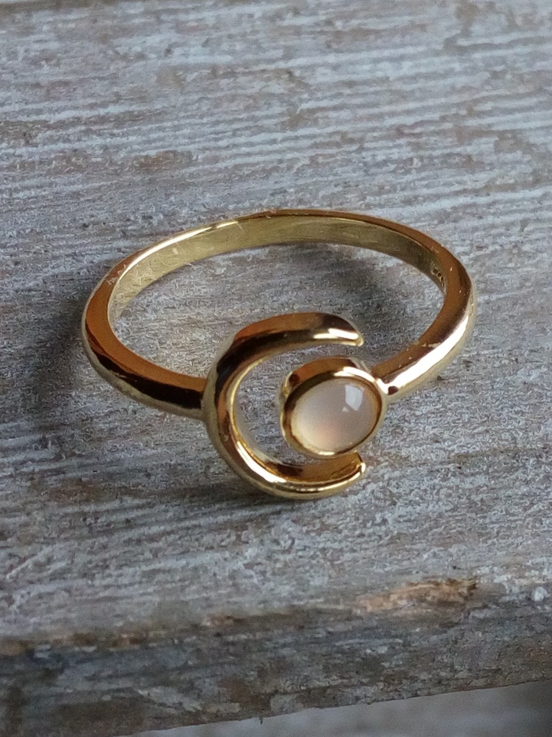 May include: A gold ring with a crescent moon design and a white gemstone in the center.