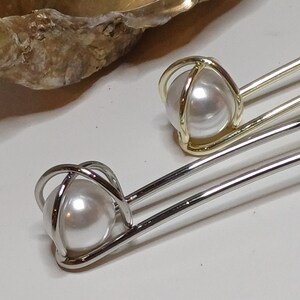 Puede incluir: Dos pinzas para el pelo plateadas con una perla en un dise&ntilde;o de jaula. La perla es blanca y la jaula es de metal plateado.