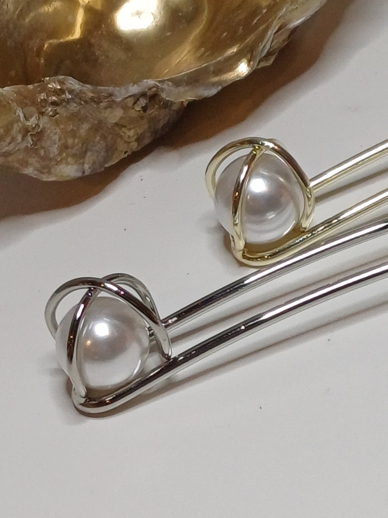 Puede incluir: Dos pinzas para el pelo plateadas con una perla en un dise&ntilde;o de jaula. La perla es blanca y la jaula es de metal plateado.