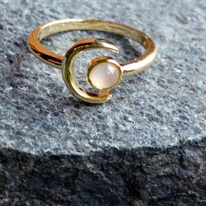 May include: A gold ring with a crescent moon design and a white stone in the center.