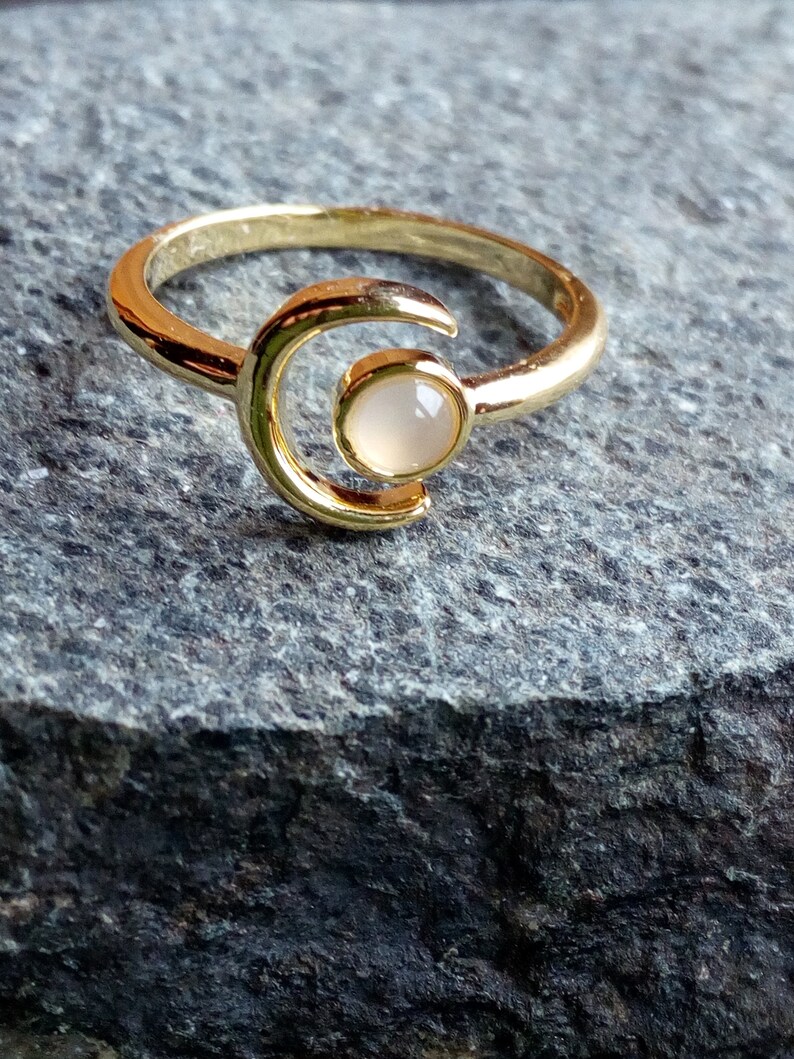 May include: A gold ring with a crescent moon design and a white stone in the center.