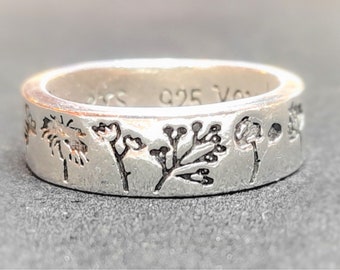 May include: A silver band ring with a textured surface and a design of five different floral motifs. The ring is engraved with the text "925" on the inside.
