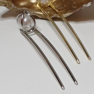 Puede incluir: Dos pinzas para el pelo con detalles de perlas. Una pinza es plateada y la otra es dorada.