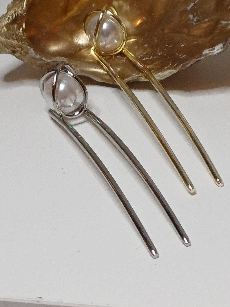 Puede incluir: Dos pinzas para el pelo con detalles de perlas. Una pinza es plateada y la otra es dorada.
