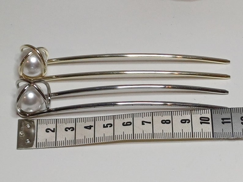 Puede incluir: Dos pinzas para el pelo con detalles de perlas. Las pinzas son de metal y tienen un acabado dorado y plateado. Las pinzas miden aproximadamente 12,5 cm de largo.