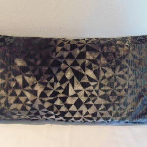 May include: A rectangular cushion with a geometric pattern in shades of green, black, and white. The cushion is made of a soft, velvety fabric.