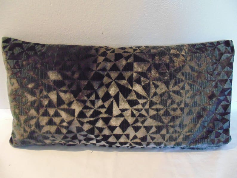 May include: A rectangular cushion with a geometric pattern in shades of green, black, and white. The cushion is made of a soft, velvety fabric.
