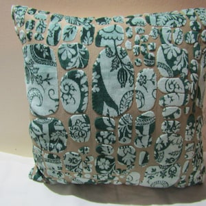 Puede incluir: Una almohada decorativa con fondo beige y un patrón floral verde y azul. El patrón está formado por formas repetidas que se asemejan a guijarros.