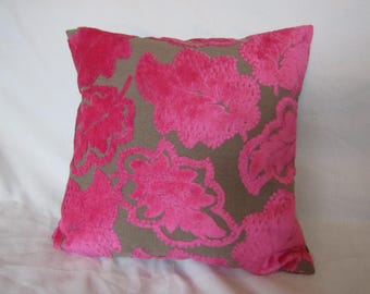 Pode incluir: Uma almofada decorativa quadrada com um padrão floral rosa sobre um fundo taupe. A almofada tem uma textura macia e aveludada, ideal para decoração de interiores.