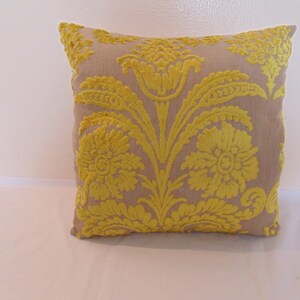 May include: A beige throw pillow with a yellow floral pattern. The pillow has a square shape and is made of a soft, textured fabric.