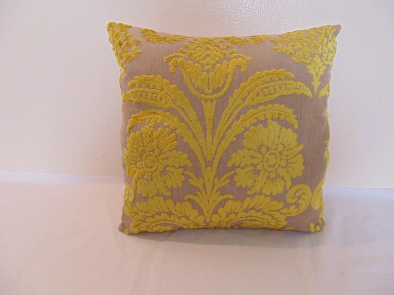 May include: A beige throw pillow with a yellow floral pattern. The pillow has a square shape and is made of a soft, textured fabric.