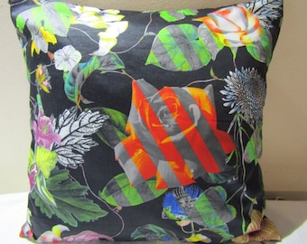 May include: A black pillow with a colorful floral print featuring roses, leaves, and other flowers. The roses are red, orange, and white with black stripes. The leaves are green and black.