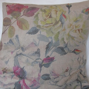 Puede incluir: Cojín cuadrado decorativo con estampado floral. El cojín presenta un fondo beige adornado con rosas estilo acuarela en tonos rosa, amarillo y blanco, con hojas verdes y grises. La tela parece ser lino o similar.