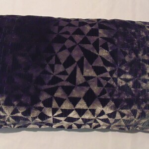 May include: A decorative cushion with a geometric pattern in shades of grey and purple. The cushion is made of a soft, velvety fabric.