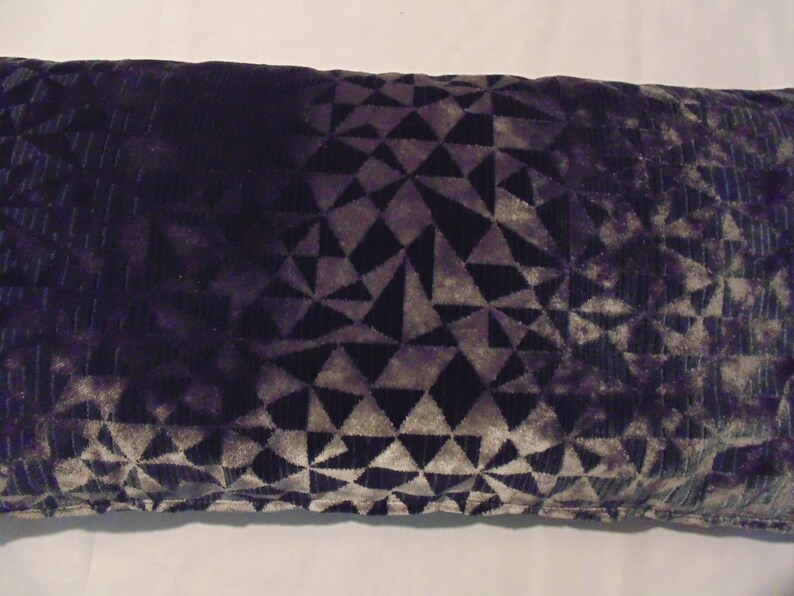 May include: A decorative cushion with a geometric pattern in shades of grey and purple. The cushion is made of a soft, velvety fabric.