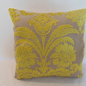 May include: A beige throw pillow with a yellow floral pattern. The pillow has a damask design with a raised texture.
