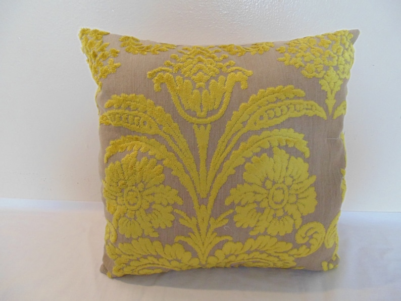 May include: A beige throw pillow with a yellow floral pattern. The pillow has a damask design with a raised texture.