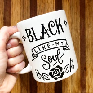A white mug with black text and graphics on it.
