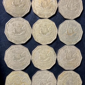 Könnte beinhalten: Eine Sammlung von zwölf zwölfeckigen Ein-Dollar-Münzen aus Belize. Elf Münzen zeigen ein Segelschiff mit der Aufschrift ONE DOLLAR $1 BELIZE und verschiedenen Jahreszahlen. Eine Münze zeigt das Profil von Königin Elizabeth II. mit der Aufschrift QUEEN ELIZABETH THE SECOND.