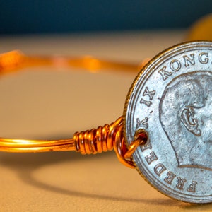 May include: A copper wire bracelet with two silver coins attached. The coins feature a profile of a man with the text "KONGE AF DANMARK FREDERIK IX" around the edge.