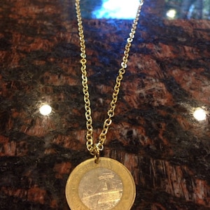 May include: A gold chain necklace with a round coin pendant featuring a silver image of a building. The coin is slightly tarnished.